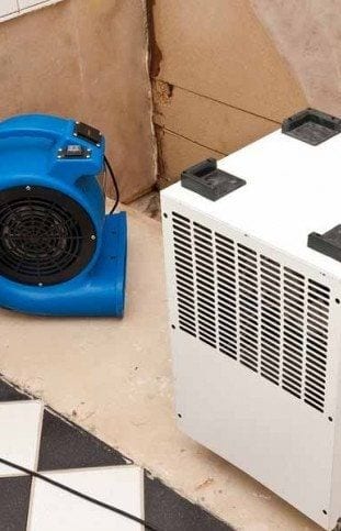 A blue air mover and a white dehumidifier drying out a water-damaged room