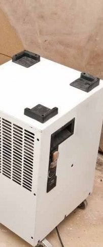 A white portable dehumidifier standing in a damaged room