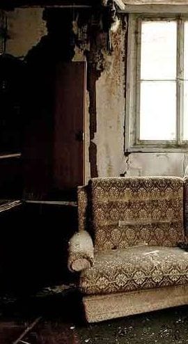 A fire-damaged room with burnt walls, a sofa and a window
