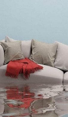 A flooded room with a grey sofa and red throw standing in water