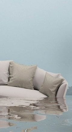 A grey sofa standing in floodwater against a teal wall