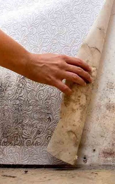 A hand peeling back mouldy wallpaper to reveal a stained, damp wall